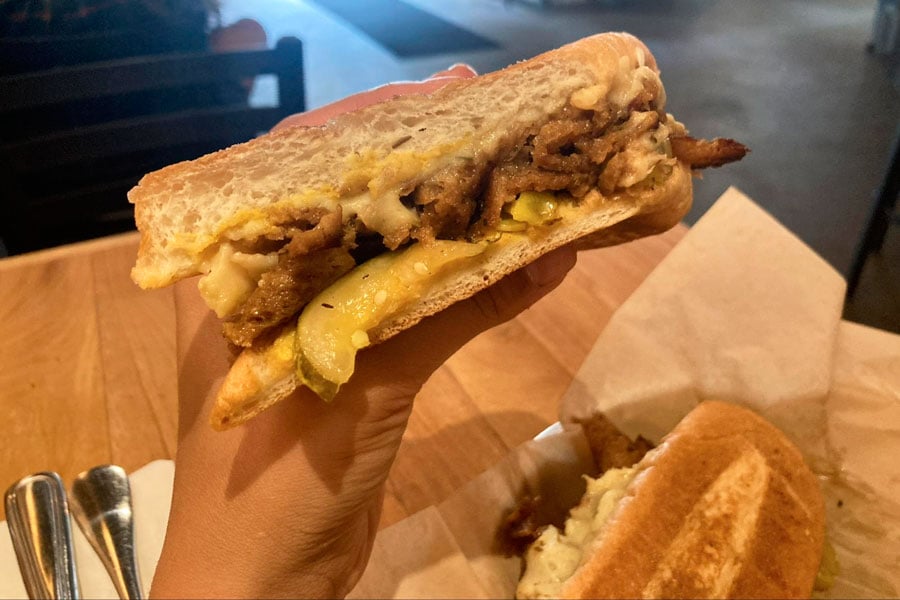 Una mano sosteniendo un sándwich cubano para veganos en Watercourse Foods