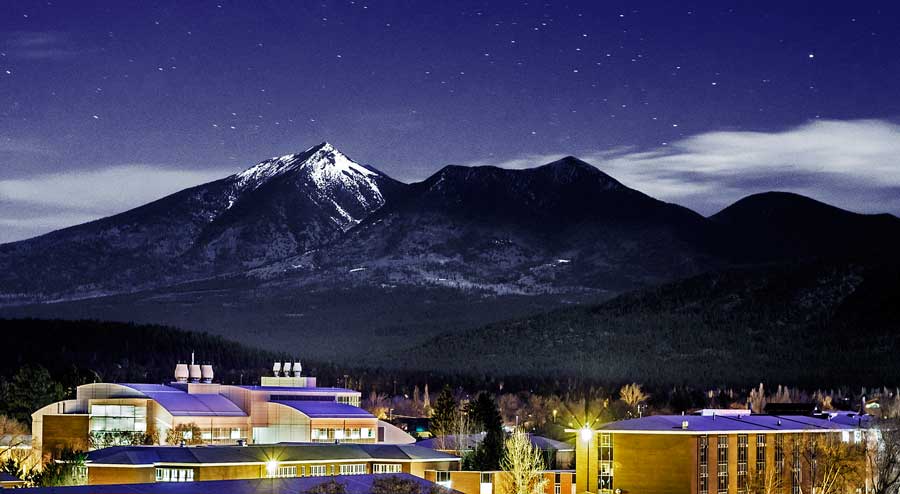 El campus de la NAU bajo la noche estrellada y una montaña nevada de fondo en Flagstaff
