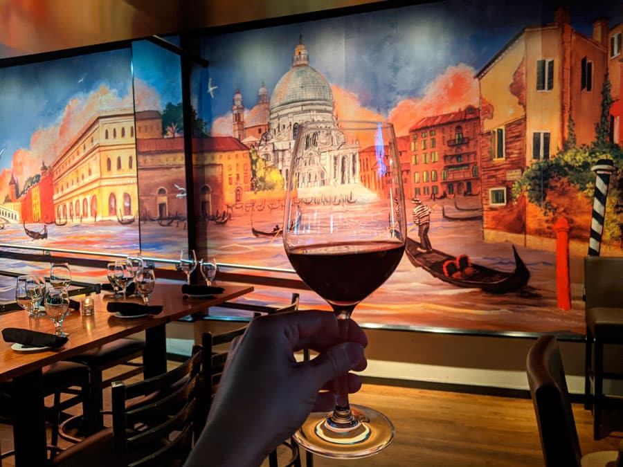 Una mano sosteniendo una copa de vino y un mural en su fondo dentro de Venice Ristorante
